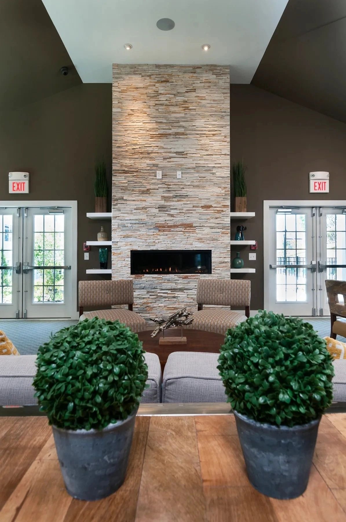 A residential-community clubhouse great room with a stacked-stone fireplace, soft seating and topiaries.